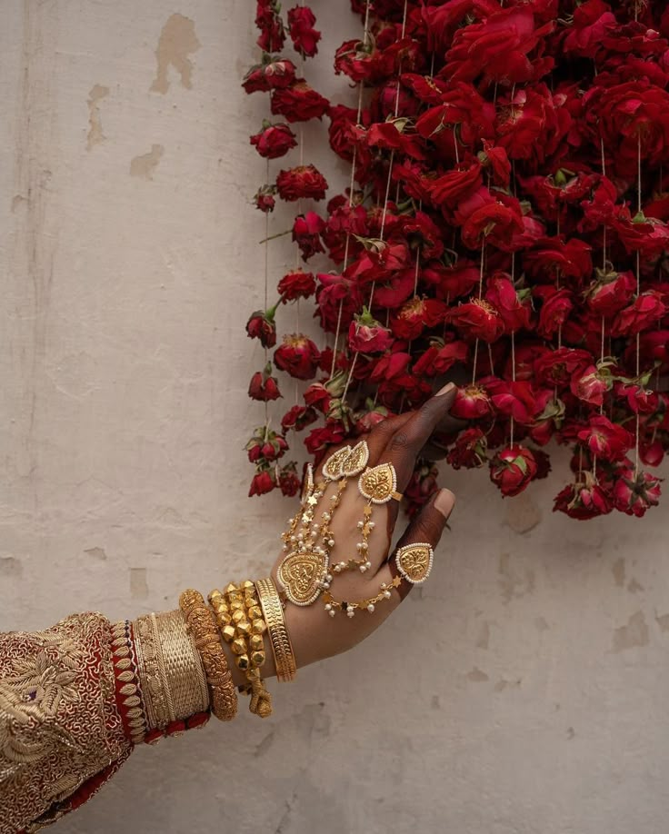 a woman in gold bracelets and red dress holding a knife with flowers on the wall behind her