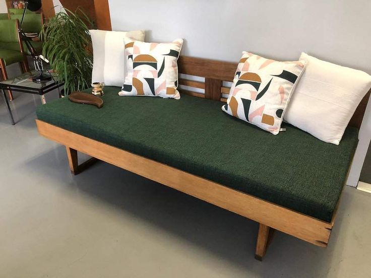 a wooden bench with two pillows on it and a plant in the corner next to it