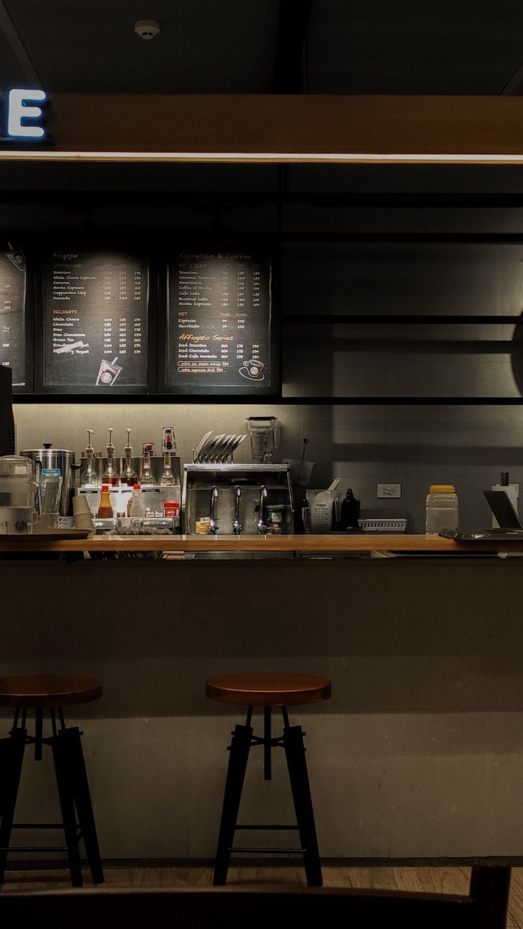 two stools sit in front of a counter with menus on the wall behind it