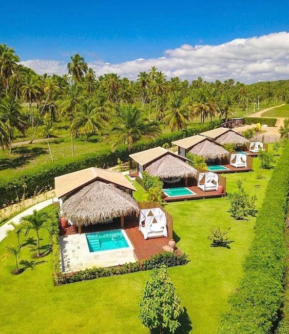 an aerial view of a resort with swimming pool and thatched roof huts, surrounded by palm trees