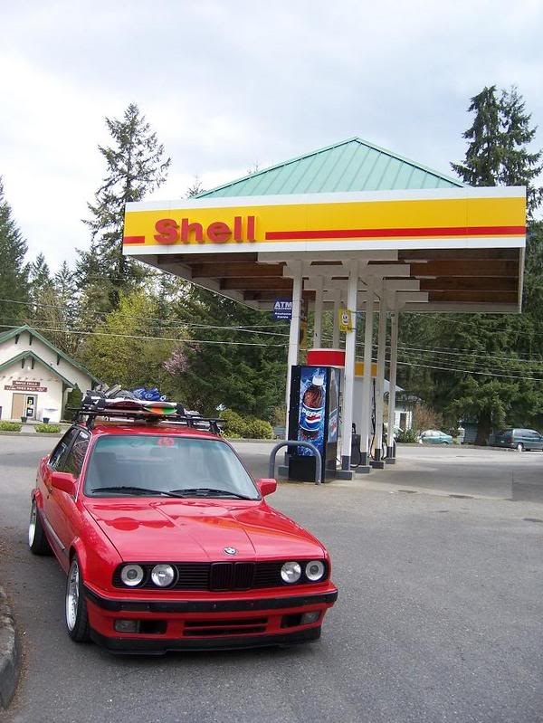 a red car is parked in front of a shell gas station with its hood up