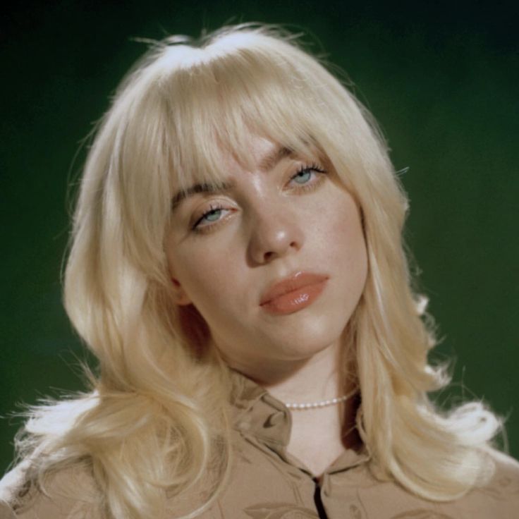 a woman with blonde hair and blue eyes is posing for a photo in front of a green background