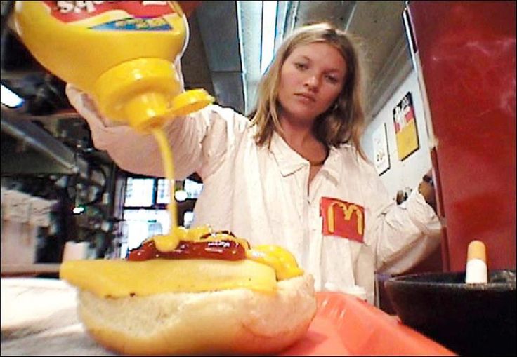 a woman pouring ketchup onto a hot dog in a bun with mustard on it