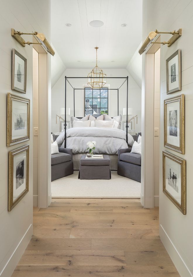 a bedroom with white walls and wood flooring, framed pictures on the wall above the bed