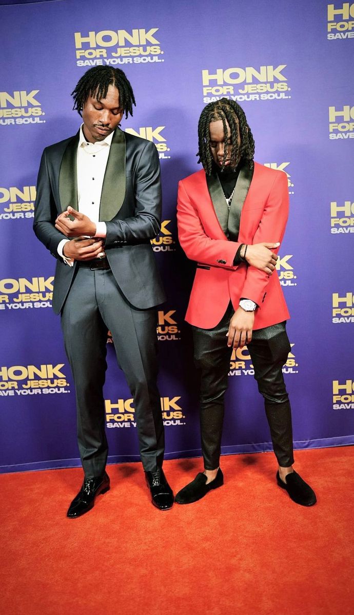 two men standing next to each other in front of a red carpet and blue wall