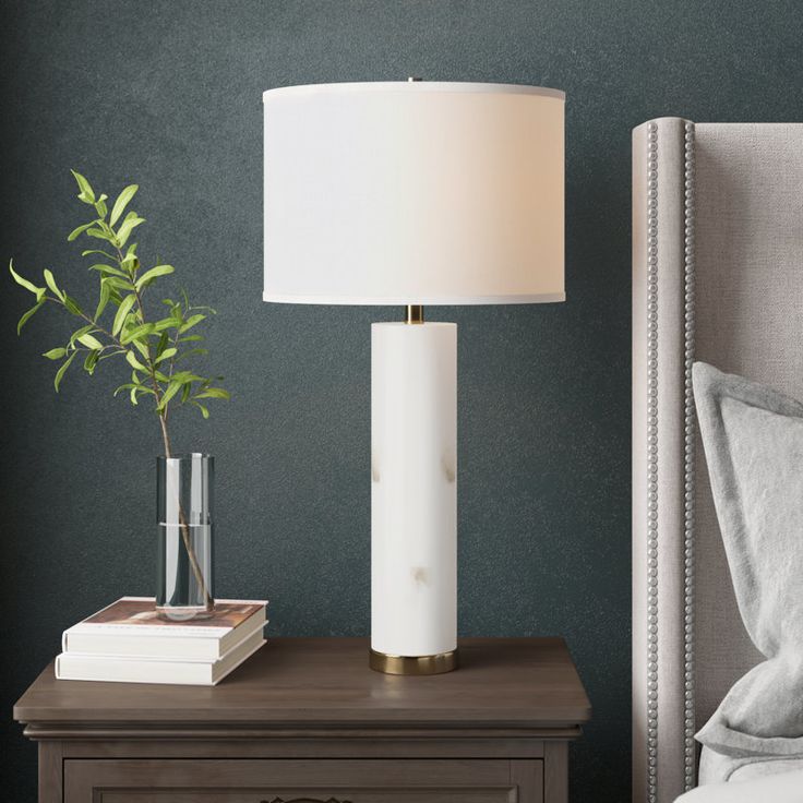 a white lamp sitting on top of a wooden table next to a night stand with a plant