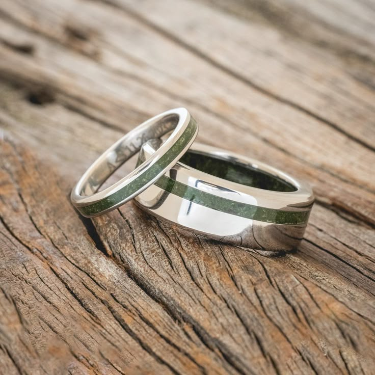 two wedding rings sitting on top of a wooden table next to each other with green stripes