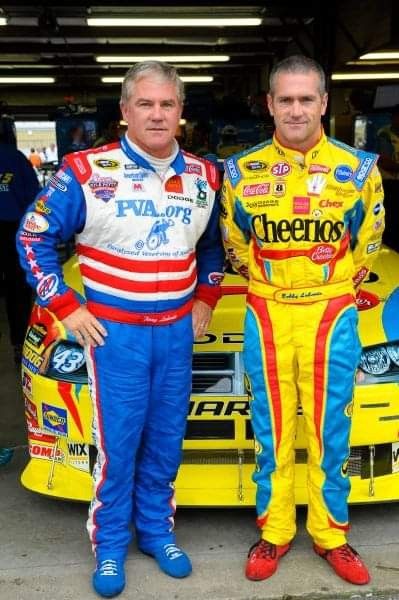 two men standing next to each other in front of a race car