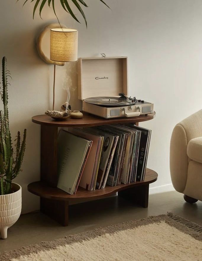 a record player sitting on top of a wooden shelf next to a chair and potted plant