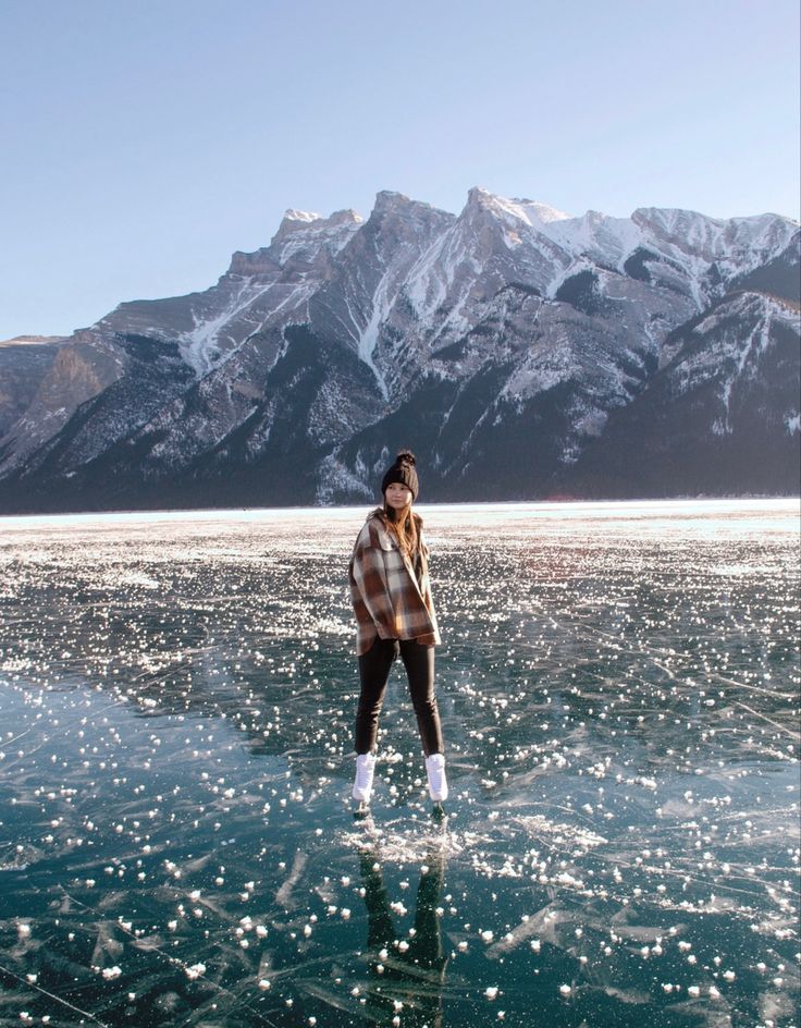 a woman standing in the middle of water with mountains in the backgroung