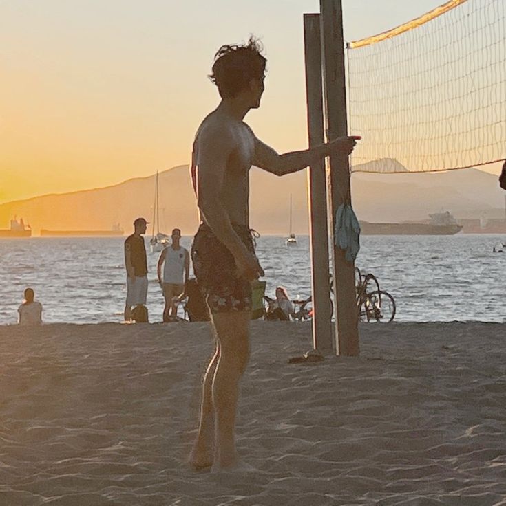 a man standing on top of a sandy beach next to a volleyball ball near the ocean