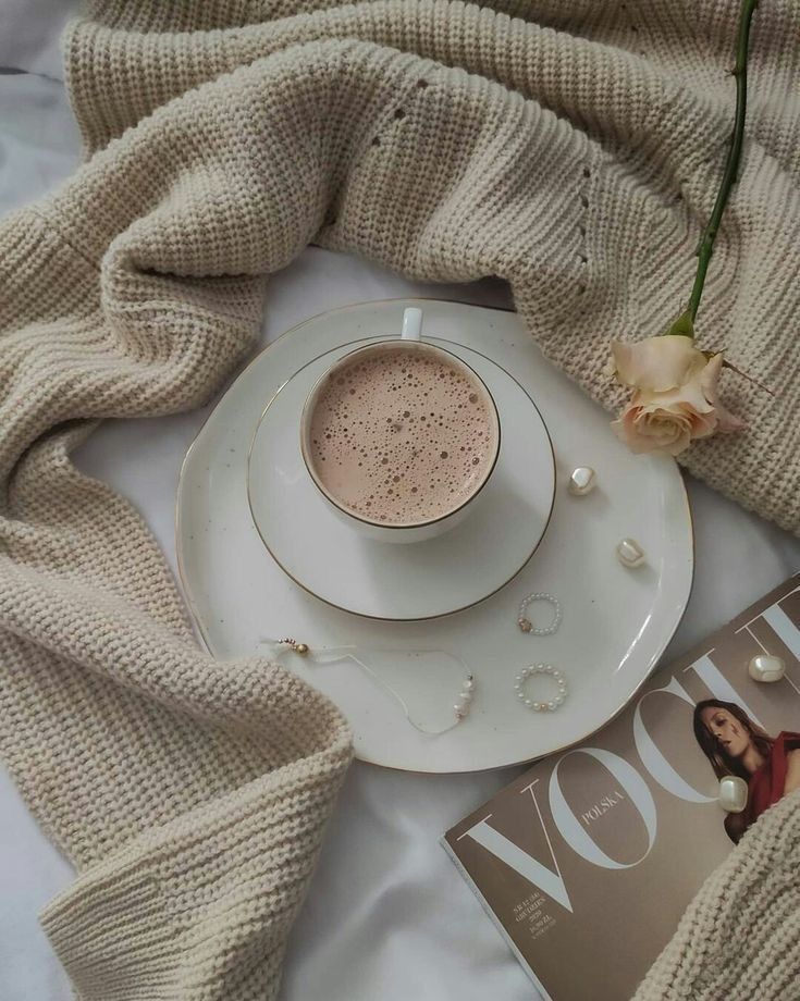 a white plate topped with a cup of coffee next to a magazine and a rose