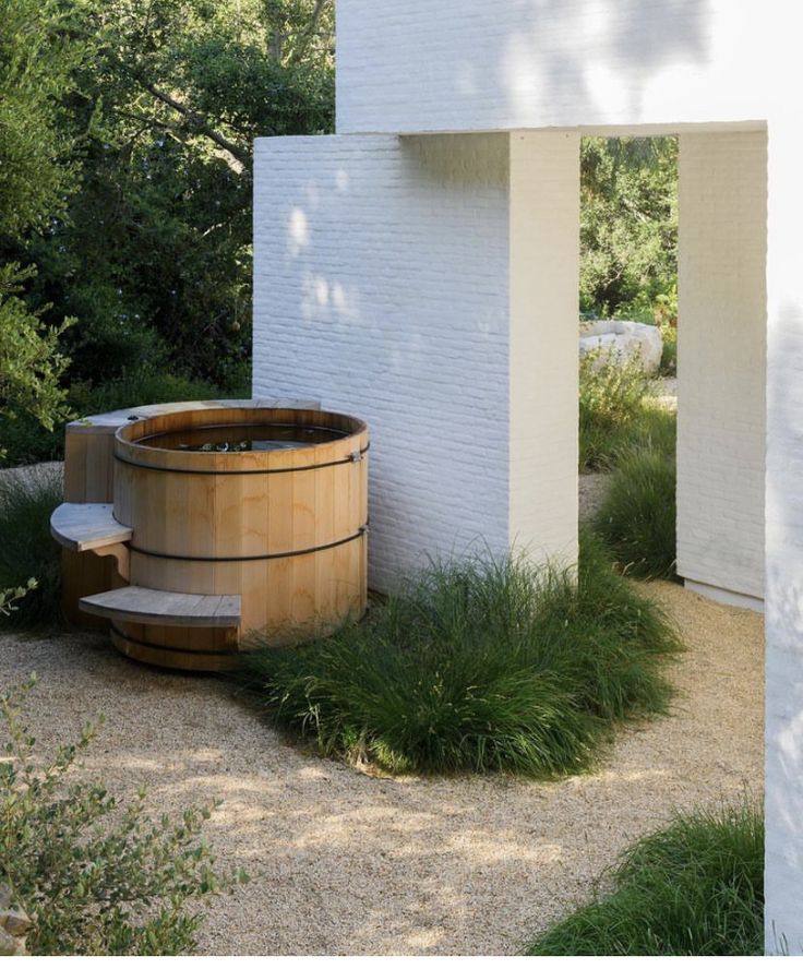 a large wooden tub sitting in the middle of a lush green field next to a white building