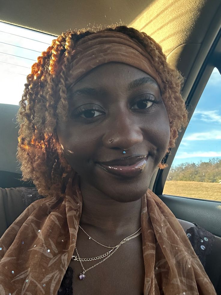 a woman with curly hair and piercings in a car looking at the camera smiling