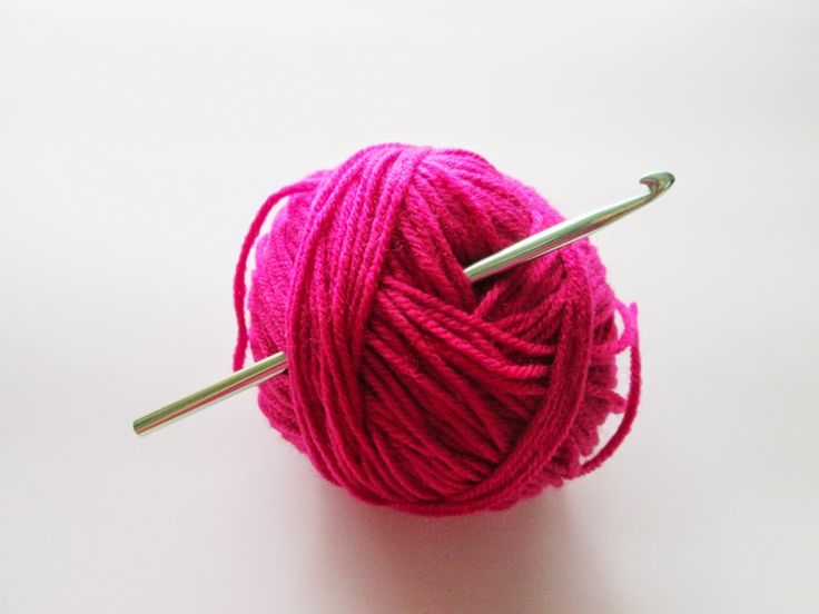 a ball of yarn with two knitting needles in front of it on a white surface