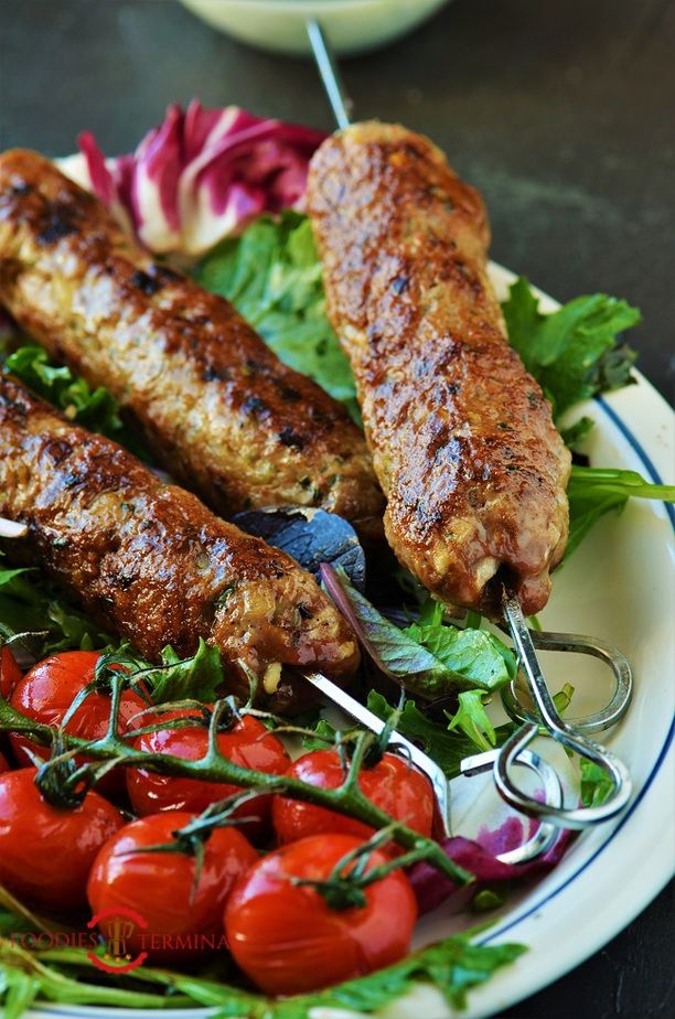 two meat skewers on a plate with tomatoes and lettuce