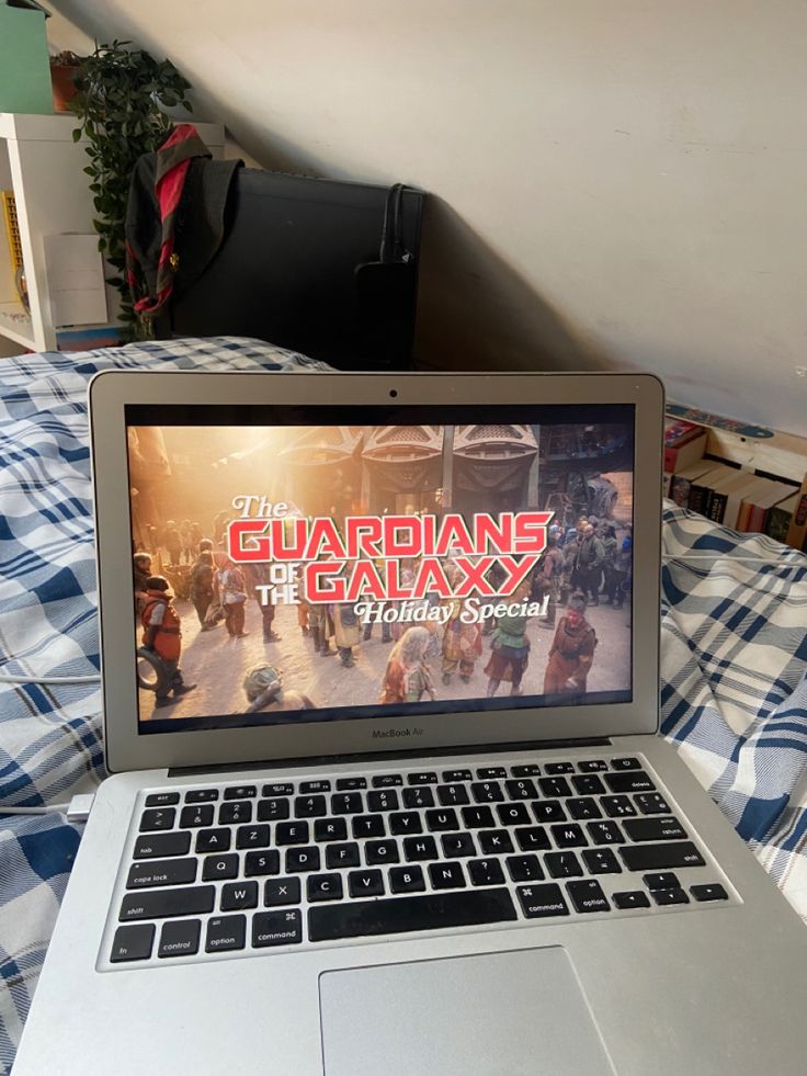 an open laptop computer sitting on top of a bed next to a plaid bedspread