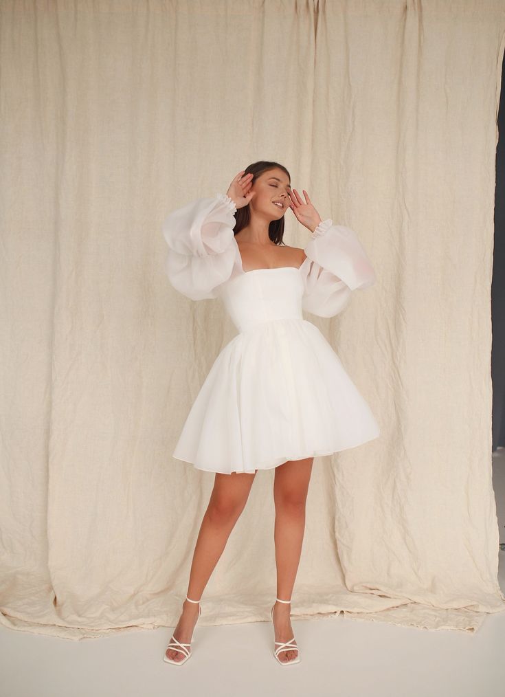 a woman in a white dress posing for the camera with her hands behind her head