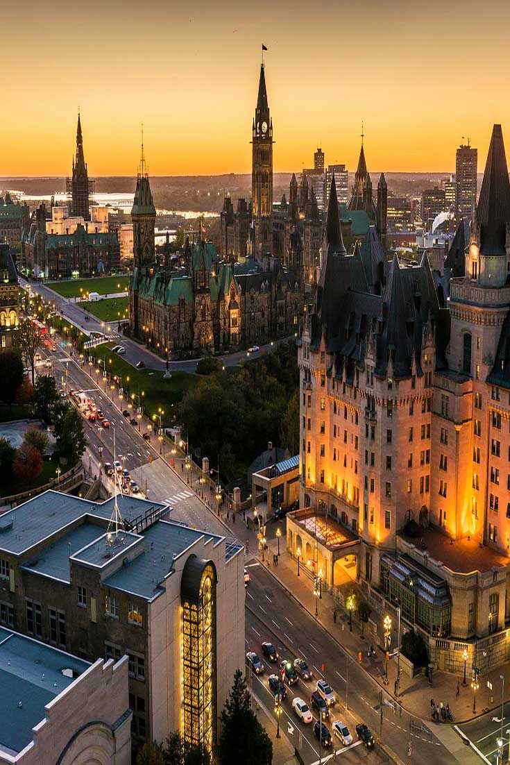 an aerial view of a city at dusk with the sun setting in the background and buildings lit up