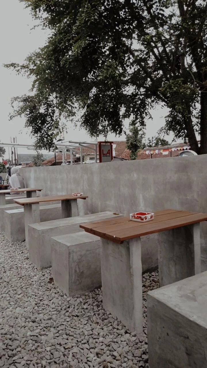 several concrete benches are lined up against a cement wall with a tree in the background