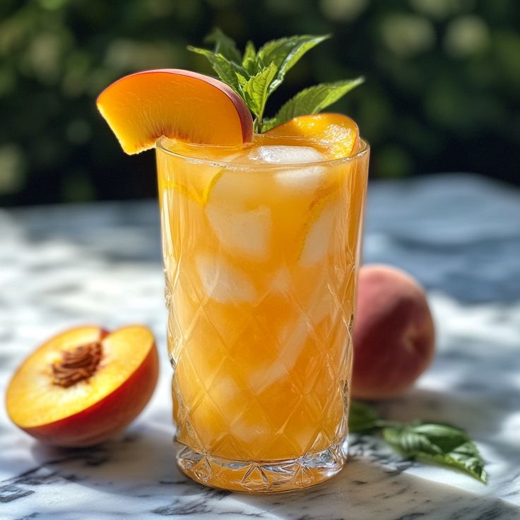 a glass filled with orange juice and garnish next to peaches on a table