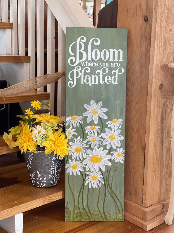 a wooden sign that says bloom when you are planted with daisies in the foreground