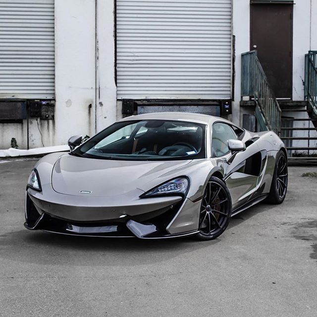 a silver sports car parked in front of a building with roller doors on it's side