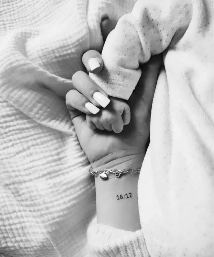 a woman holding her baby's hand while she is wearing a bracelet with the number thirteen on it