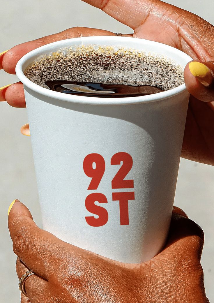 a woman holding up a cup of coffee with the number 921 st on it