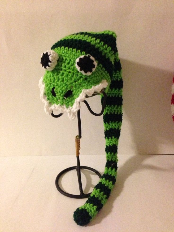 a crocheted green and white hat with black eyeballs on the top, attached to a hook