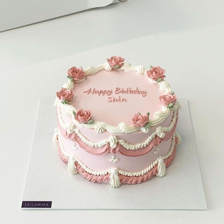 a pink and white birthday cake with roses on it