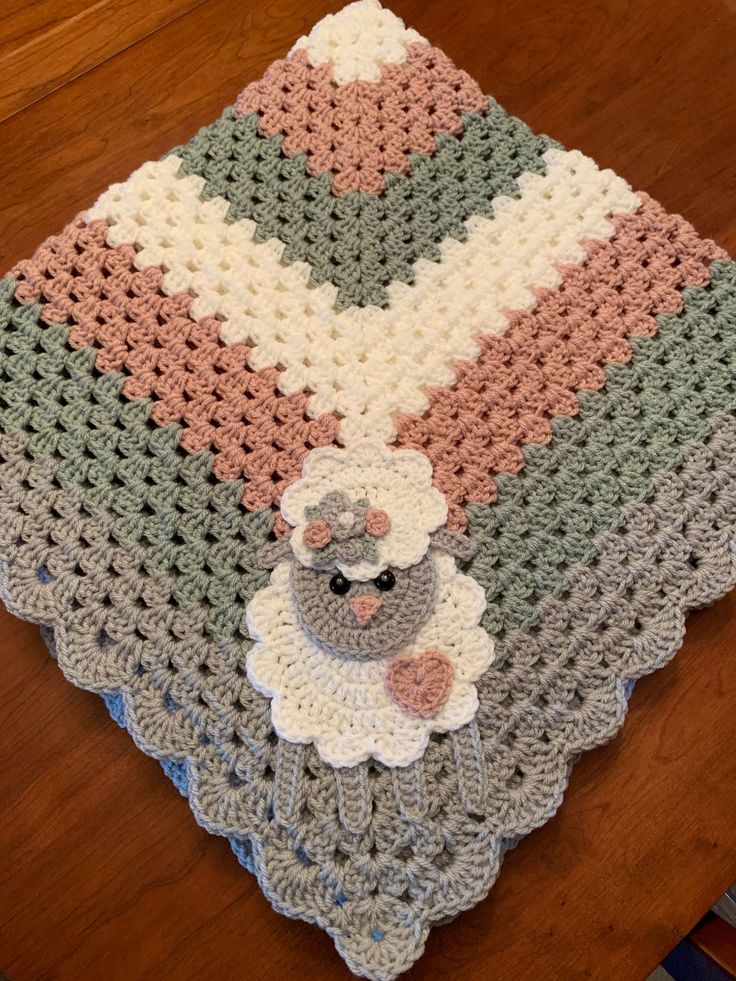 a crocheted blanket with a teddy bear on it sitting on a wooden table