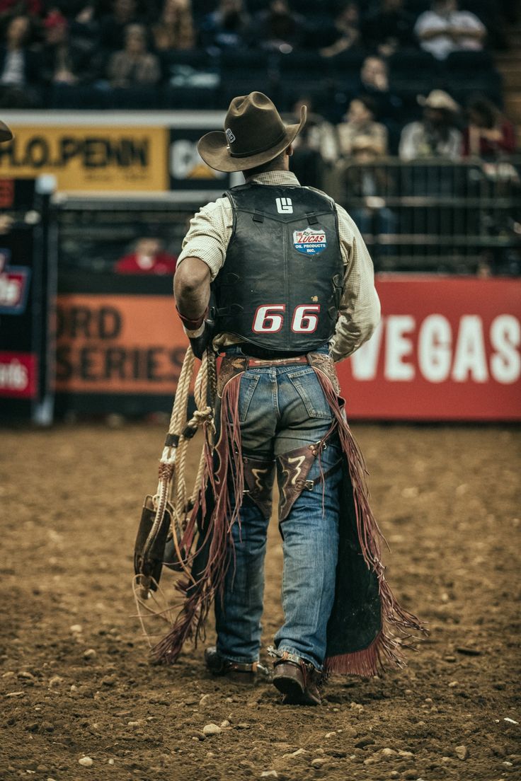 a man with a cowboy hat and lasso walking in the dirt at a rodeo