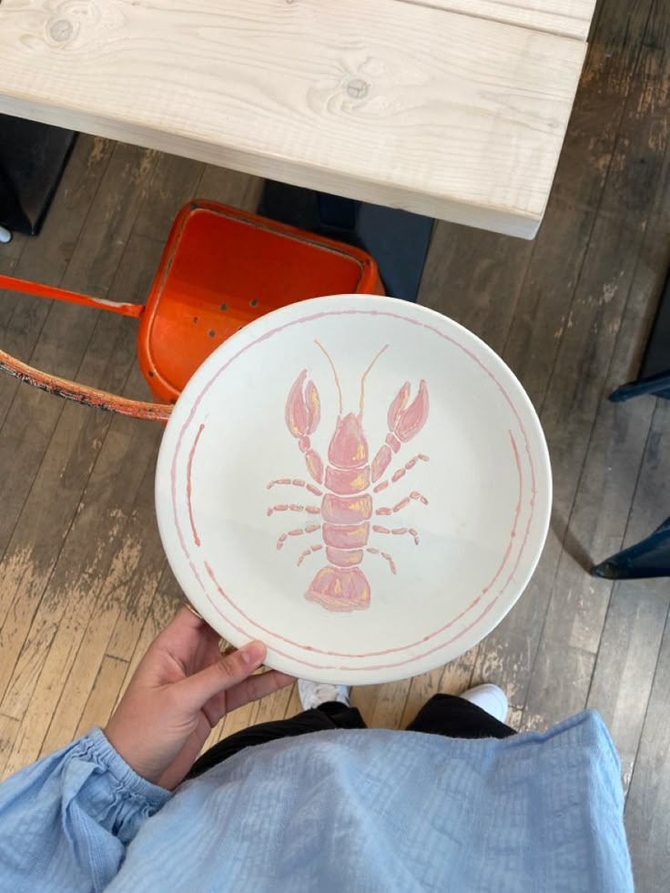 a person holding up a plate with a lobster painted on the front and side of it