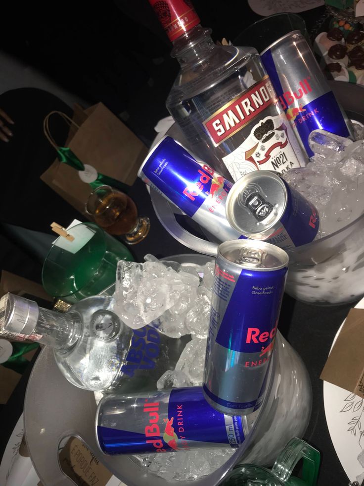 two bottles of red bull are sitting on top of some ice cubes and glasses