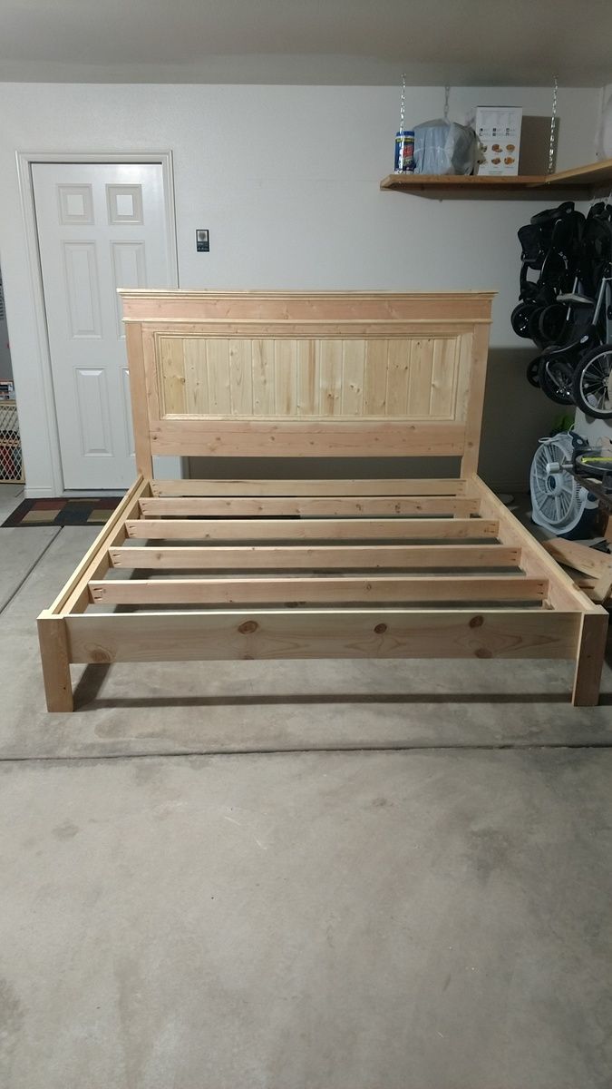 a bed frame made out of wood sitting in a room next to a door and shelves