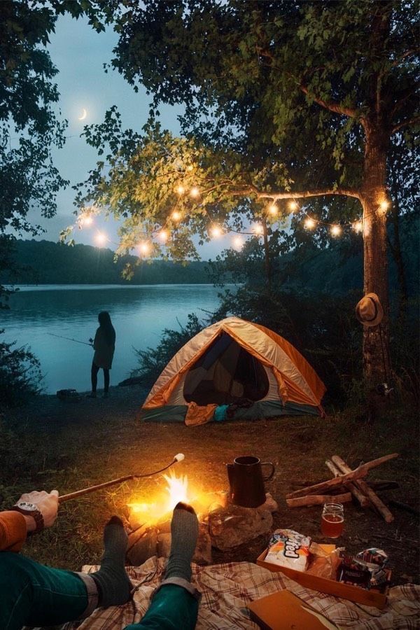 two people are camping in the woods at night with lights strung from trees over them