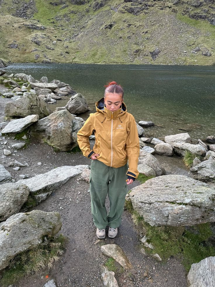 a woman standing on top of a rocky hill next to a lake