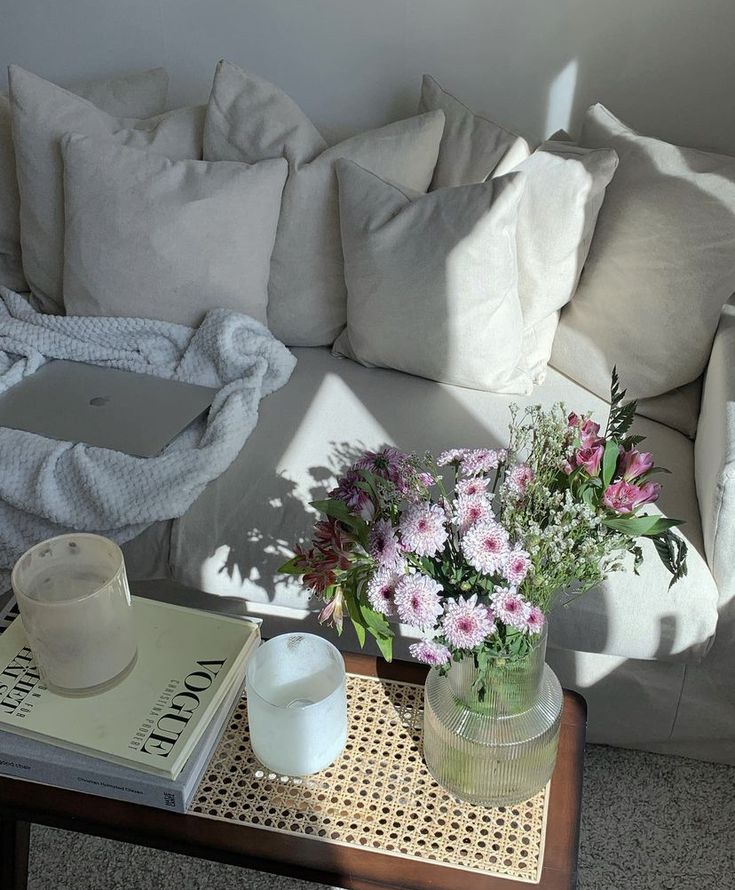 A white couch coating in sunlight. There’s a coffee table with hooks, candles, and a vase of flowers. Apartment Decor Clean Aesthetic, Aesthetic White Apartment, Own Home Aesthetic, Clean Girl House Decor, White Aesthetic Apartment, White Cozy Apartment, Simple Apartment Aesthetic Living Room, Clean Aesthetic House, Apartment Details Aesthetic