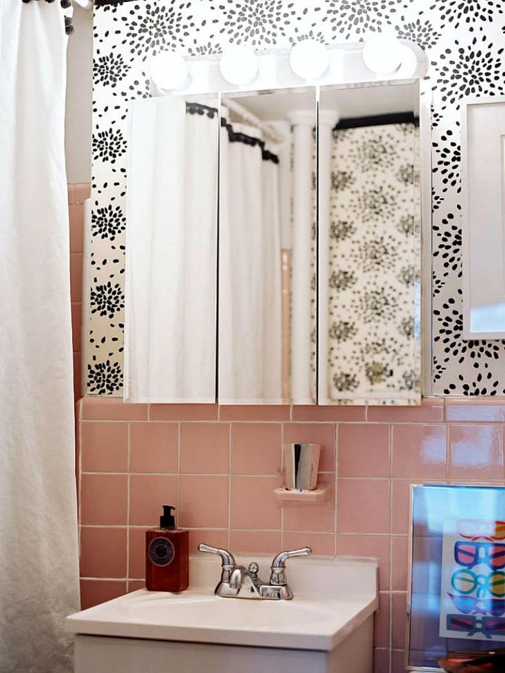 a bathroom with pink tiles and white fixtures, including a mirror above the sink that has black flowers on it