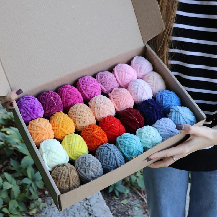 a woman is holding a box full of balls of yarn in it's hands