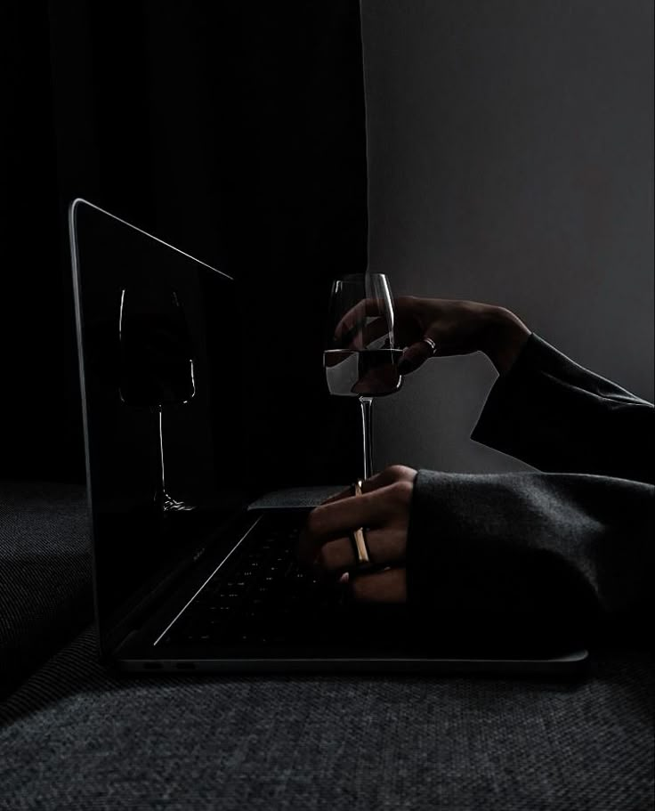 a person holding a wine glass while using a laptop