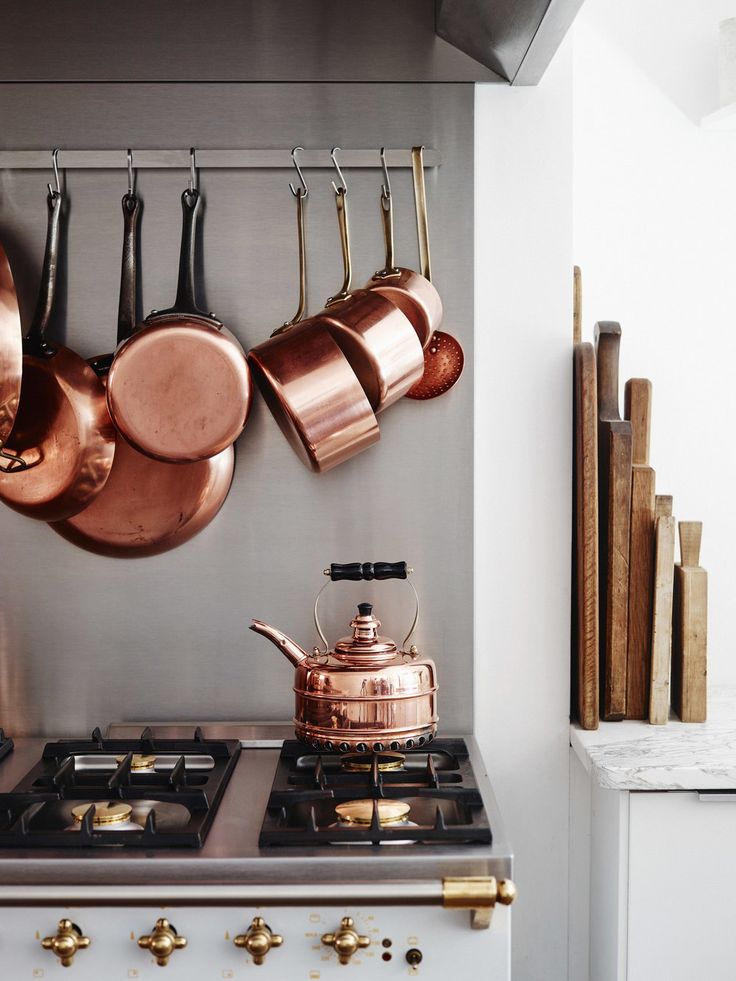 pots and pans are hanging on the wall above an oven with two burners