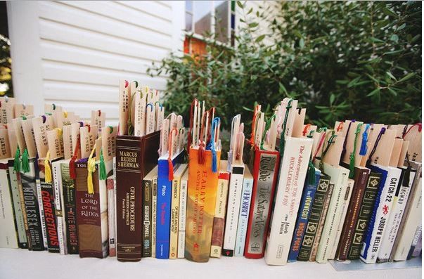 a row of books sitting on top of a white table next to a green tree