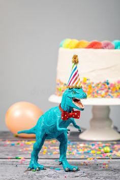 a toy dinosaur wearing a party hat and holding a birthday cake with sprinkles