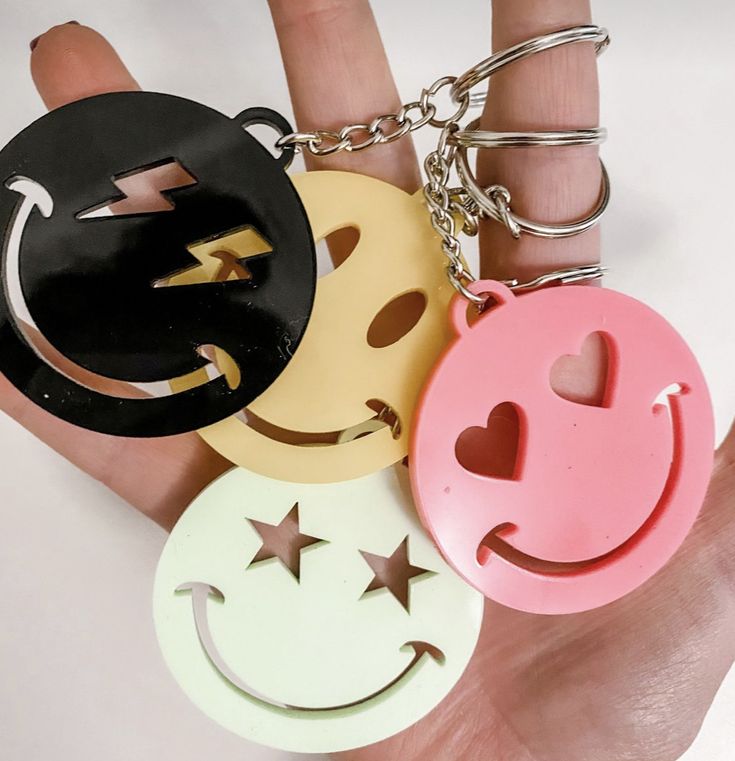 a hand holding four different colored smiley face key chains