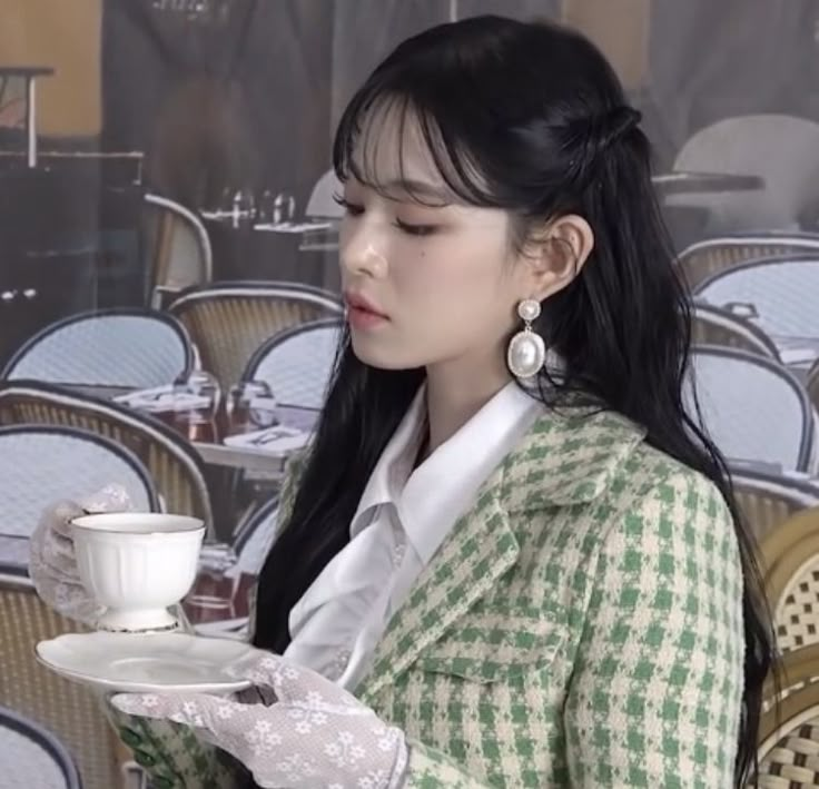 a woman holding a cup and saucer in front of a wall covered with chairs