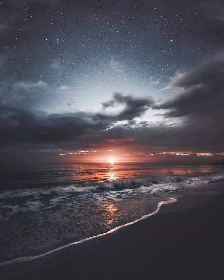 the sun is setting over the ocean with dark clouds and stars in the night sky