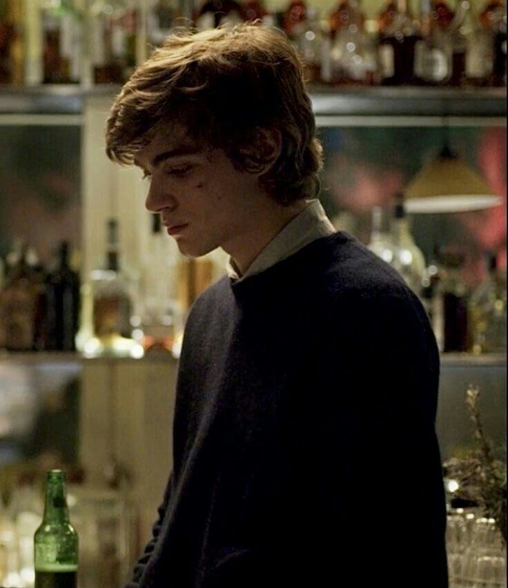 a young man standing in front of a bar with bottles on the shelves behind him