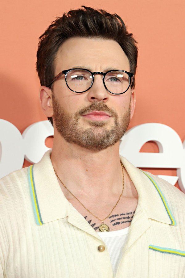 a man with glasses and a beard in front of a pink wall wearing a white shirt